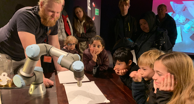 Børn på Danmarks Tekniske Museum, som prøver at tegne med en robotarm